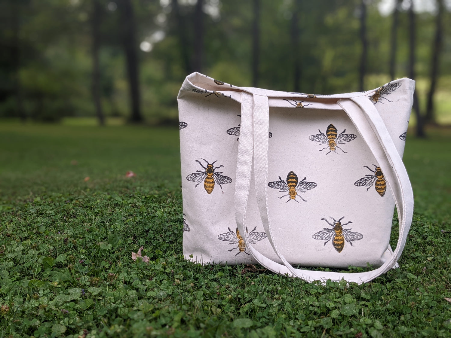 bee block printed tote bag sitting in grassy area with trees in background